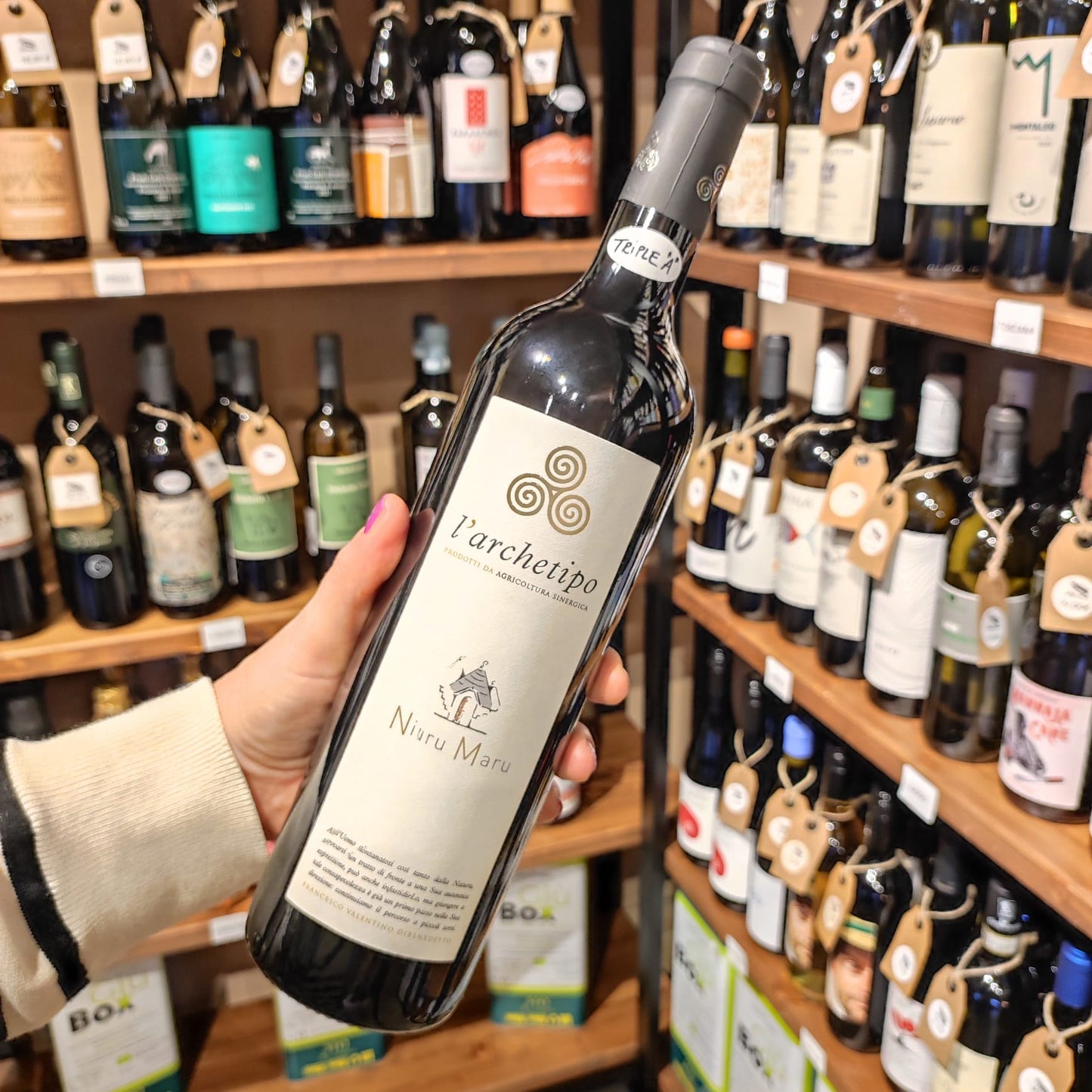 Bottiglia di Niuru Maru L’Archetipo – vino rosso naturale pugliese da agricoltura sinergica, su sfondo di scaffali